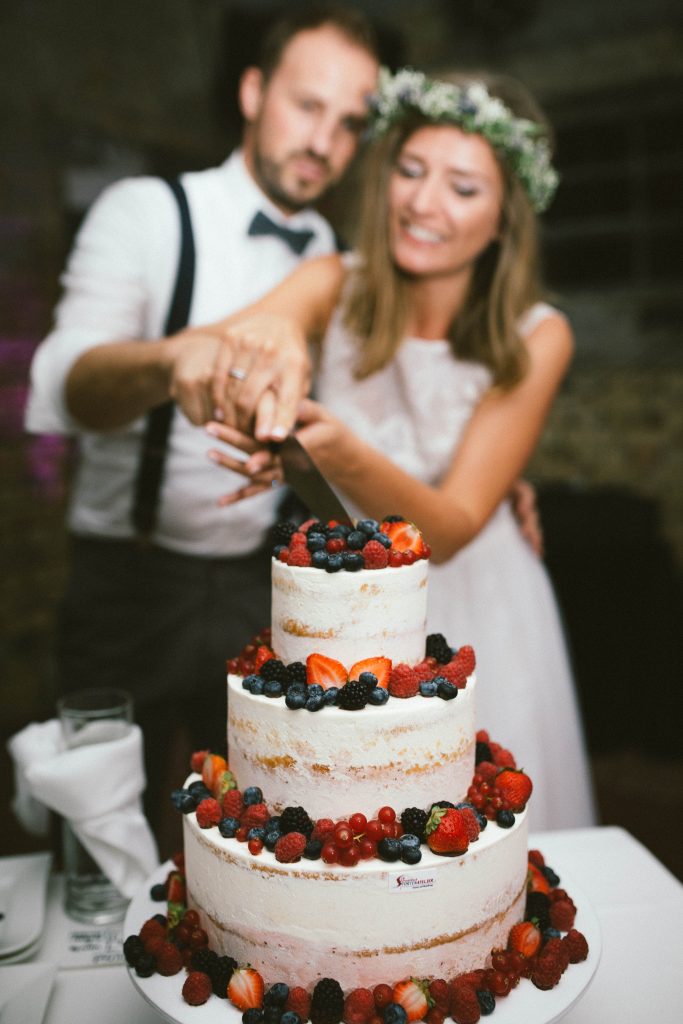Brautpaar schneidet gemeinsam eine dreistöckige Hochzeitstorte mit Beeren an